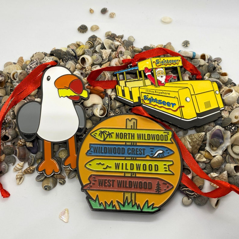 May include: A set of four colorful metal ornaments featuring the names of different locations in Wildwood, New Jersey. The ornaments are shaped like signs with a yellow background and blue, red, and green accents. The text on the signs reads "North Wildwood", "Wildwood Crest", "Wildwood", and "West Wildwood".