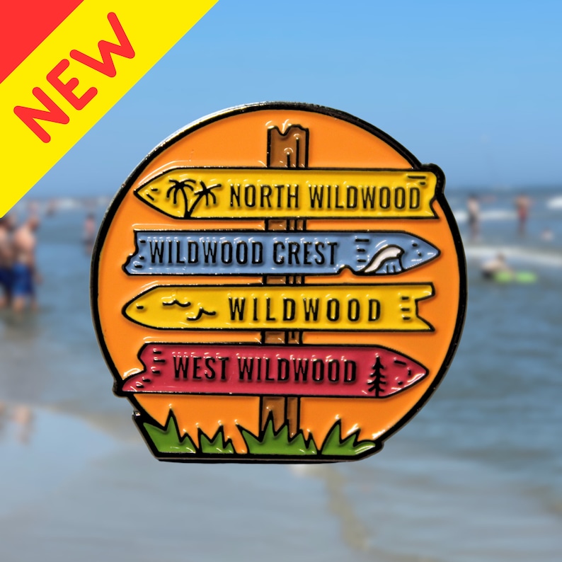 Pu&ograve; includere: Una spilla smaltata colorata con un cartello stradale con quattro frecce direzionali che puntano verso diverse localit&agrave;: North Wildwood, Wildwood Crest, Wildwood e West Wildwood. Il cartello stradale &egrave; su uno sfondo color tramonto con erba verde.