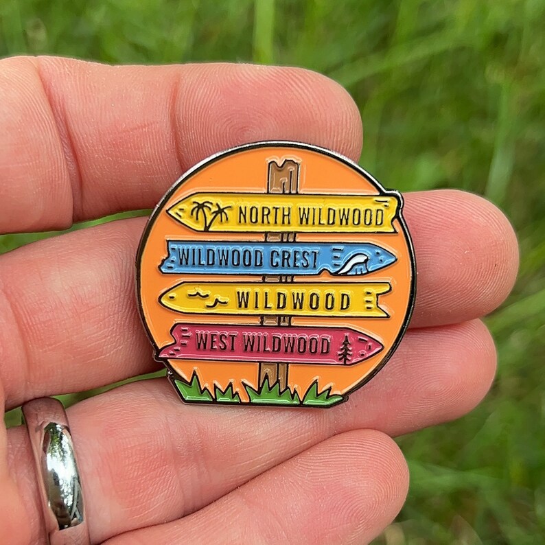 Pu&ograve; includere: Uno spillo smaltato colorato con un cartello stradale con quattro frecce direzionali che puntano a diverse localit&agrave; a Wildwood, nel New Jersey. Le frecce sono etichettate "North Wildwood", "Wildwood Crest", "Wildwood" e "West Wildwood".