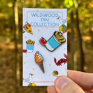 Op de afbeelding: Een set van vijf emaillepins met verschillende ontwerpen met als thema Wildwood, New Jersey. De pins bevatten een pizza-punt, een bakje friet, een softijshoorn, een krab met een zonnebril en een meeuw.