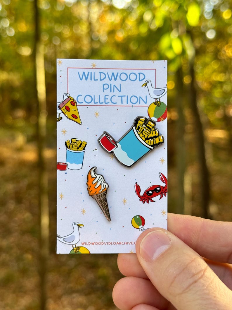 Op de afbeelding: Een set van vijf emaillepins met verschillende ontwerpen met als thema Wildwood, New Jersey. De pins bevatten een pizza-punt, een bakje friet, een softijshoorn, een krab met een zonnebril en een meeuw.