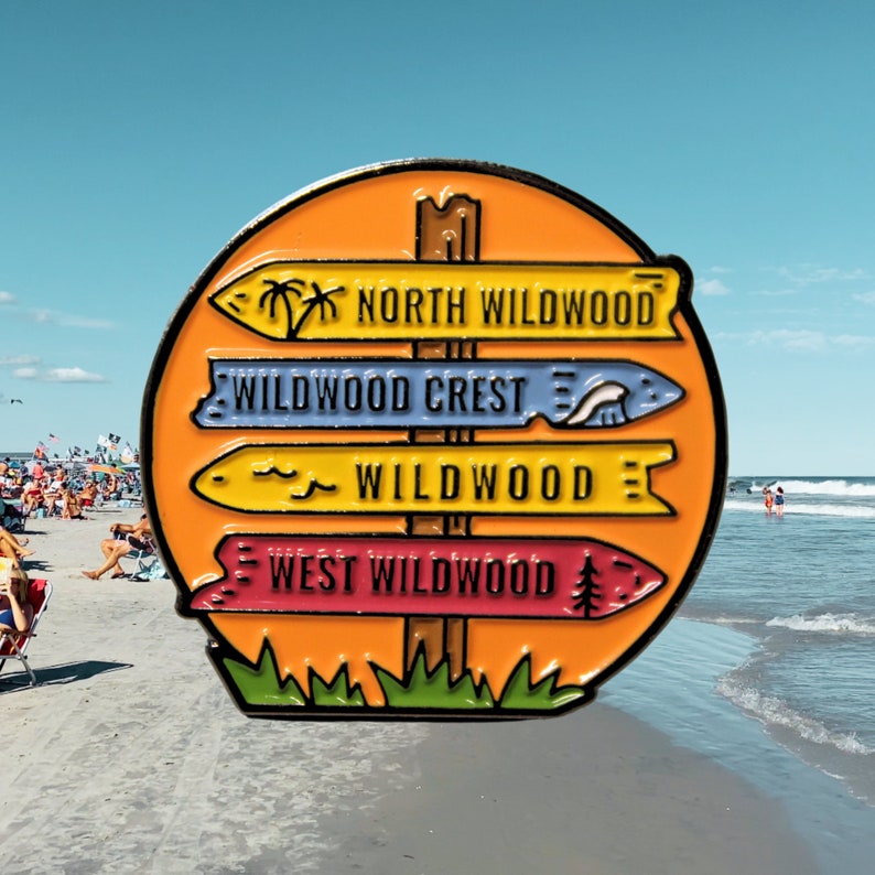 Pu&ograve; includere: Uno spillo smaltato colorato che presenta un cartello stradale con quattro frecce direzionali che puntano a diverse localit&agrave;: North Wildwood, Wildwood Crest, Wildwood e West Wildwood. Il cartello stradale &egrave; su uno sfondo color tramonto con erba verde alla base.