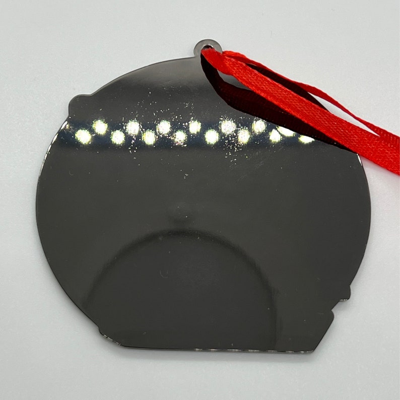 May include: A black, round, flat ornament with a red ribbon attached. The ornament has a shiny, reflective surface.