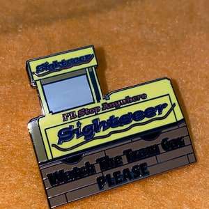 Puede incluir: Un pin de esmalte amarillo y marr&oacute;n con forma de tranv&iacute;a tur&iacute;stico. El pin tiene la palabra "Sightseer" en azul y el texto "I'll Stop Anywhere" y "Watch The Tram Car PLEASE".
