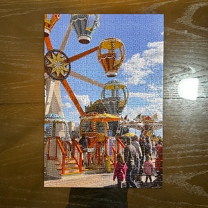 May include: A colorful carnival ride with a large Ferris wheel, hot air balloons, and a carousel. The ride is decorated with bright colors and lights. There are people walking around the ride, enjoying the festivities.