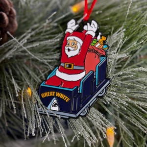 May include: A red and white Santa Claus ornament riding in a blue and white sleigh with the text "Great White" and a shark fin.