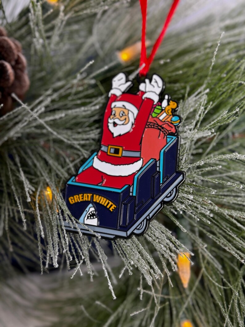 May include: A red and white Santa Claus ornament riding in a blue and white sleigh with the text "Great White" and a shark fin.