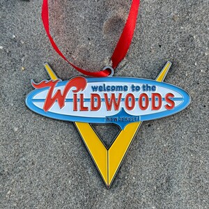 May include: A yellow, blue, and red metal ornament shaped like a surfboard with the text "Welcome to the Wildwoods New Jersey".