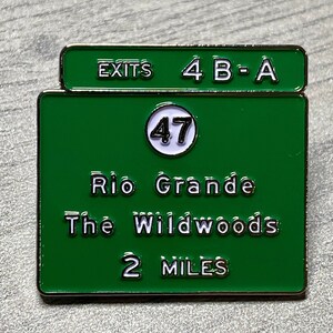 Puede incluir: Pin de esmalte verde y blanco con forma de se&ntilde;al de tr&aacute;fico. La se&ntilde;al indica "EXITS 4 B-A", "47", "Rio Grande", "The Wildwoods" y "2 MILES". El pin tiene un borde met&aacute;lico brillante.