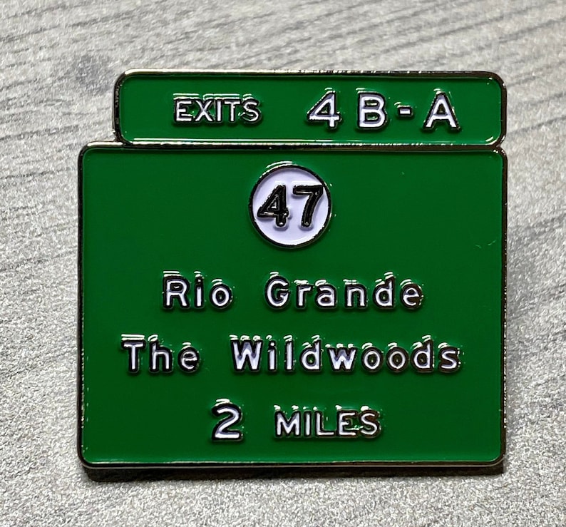 Puede incluir: Pin de esmalte verde y blanco con forma de se&ntilde;al de tr&aacute;fico. La se&ntilde;al indica "EXITS 4 B-A", "47", "Rio Grande", "The Wildwoods" y "2 MILES". El pin tiene un borde met&aacute;lico brillante.