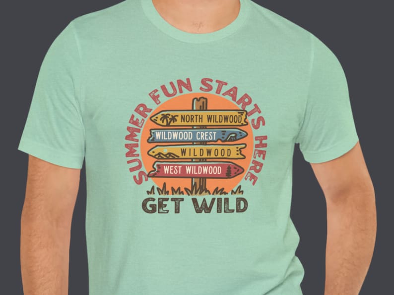 Pu&ograve; includere: T-shirt verde chiaro con grafica circolare. La grafica recita "Summer Fun Starts Here" e presenta un palo segnaletico con indicazioni per North Wildwood, Wildwood Crest, Wildwood e West Wildwood. Le parole "Get Wild" sono in basso.