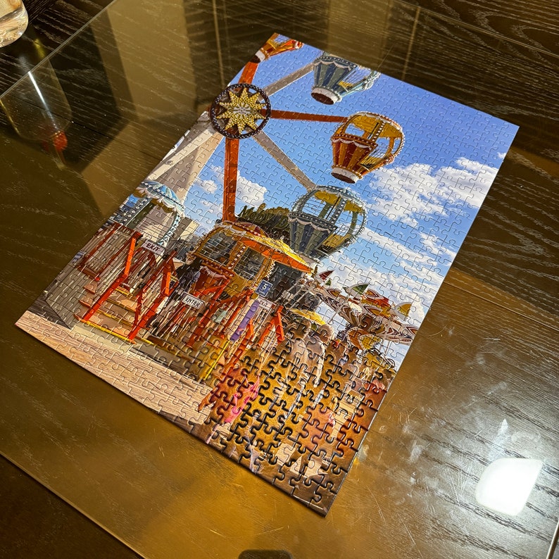 May include: A colorful jigsaw puzzle depicting a vintage carnival scene with a Ferris wheel, hot air balloons, and a carousel. The puzzle pieces are arranged in a random pattern, creating a whimsical and nostalgic feel.