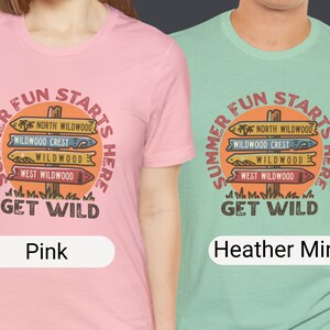 Pu&ograve; includere: T-shirt rosa e verde menta con una grafica che recita "Summer Fun Starts Here" attorno a un cartello stradale con nomi di destinazioni. Le magliette sono a girocollo.