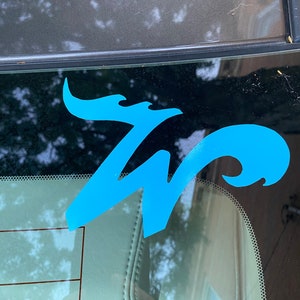 May include: A blue vinyl decal of the letter "W" with a stylized flame design. The decal is applied to a car window.