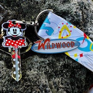 May include: A keychain with a red and white Minnie Mouse key charm, a silver Wildwood sign charm, and a green "The Wildwoods" charm. The keychain is attached to a white and blue patterned strap.