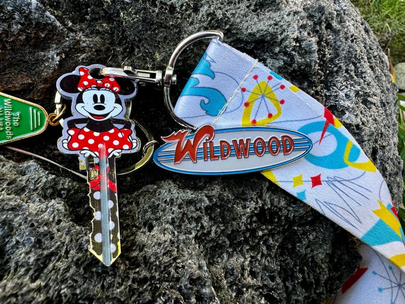 May include: A keychain with a red and white Minnie Mouse key charm, a silver Wildwood sign charm, and a green "The Wildwoods" charm. The keychain is attached to a white and blue patterned strap.