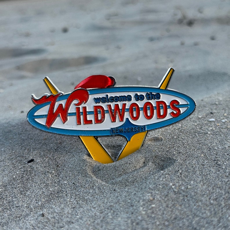 May include: A blue and white enamel pin with a red and yellow design. The pin says "Welcome to the Wildwoods, New Jersey".