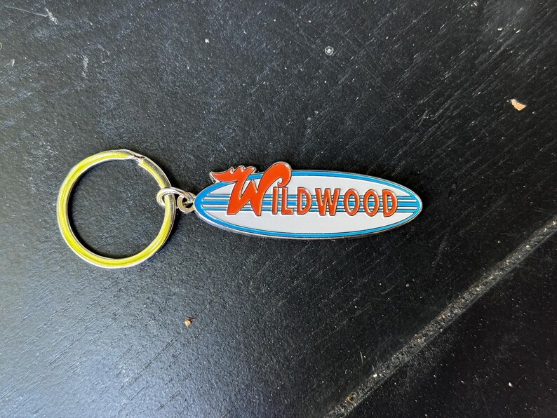 May include: A silver keychain with a yellow key ring and a blue and white surfboard charm with the word "WILDWOOD" in red letters.