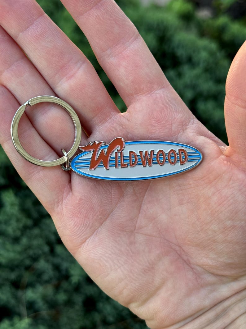 May include: A silver keychain with a blue and white surfboard-shaped charm. The charm has the word "WILDWOOD" in red letters on it.