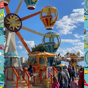 May include: A colorful Ferris wheel with gondolas shaped like hot air balloons. The Ferris wheel is on a boardwalk with people walking by. The Ferris wheel has a sign that says "Moby Dick".