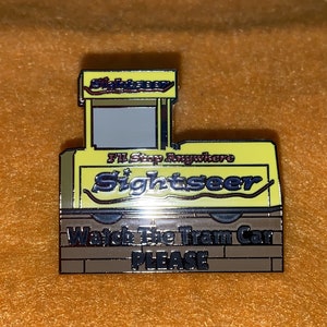 Puede incluir: Un pin de esmalte amarillo y marr&oacute;n con forma de tranv&iacute;a. El pin presenta las palabras "Sightseer" y "I'll Stop Anywhere". La parte inferior del pin dice "Watch The Tram Car PLEASE".