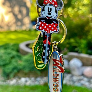 May include: A keychain with a Mickey Mouse character charm, a green and yellow charm with the text "Wildwood" and a white charm with the text "Wildwood" in blue and red lettering.
