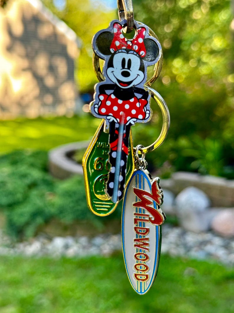 May include: A keychain with a Mickey Mouse character charm, a green and yellow charm with the text "Wildwood" and a white charm with the text "Wildwood" in blue and red lettering.