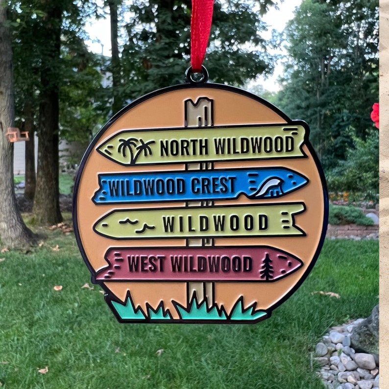 May include: A round, orange, metal sign with black trim and four directional signs pointing to different locations. The signs read "North Wildwood", "Wildwood Crest", "Wildwood", and "West Wildwood".