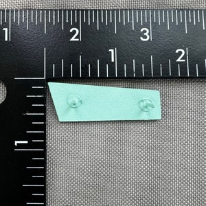 May include: A light blue metal sign with rounded corners and two silver rivets. The sign is about 2 inches long.