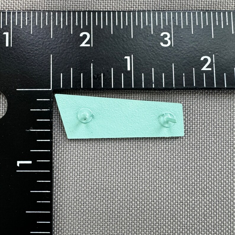 May include: A light blue metal sign with rounded corners and two silver rivets. The sign is about 2 inches long.