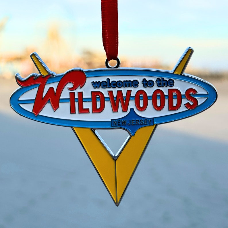 May include: A blue and white metal ornament shaped like a surfboard with the text "Welcome to the Wildwoods New Jersey". The ornament is red, white, and blue with a yellow triangle shape in the center.