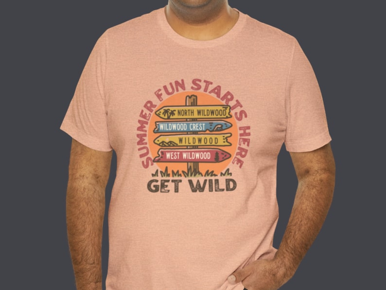 Pu&ograve; includere: Una maglietta color pesca con una grafica circolare che recita "Summer Fun Starts Here". La grafica presenta segnali direzionali che puntano a North Wildwood, Wildwood Crest, Wildwood e West Wildwood. Il testo "Get Wild" &egrave; in basso.