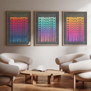 May include: Three framed art prints with the word "PENARTH" in a repeating, colorful design. The prints are displayed above a seating area with curved, cream-colored chairs and a wooden coffee table. The color schemes of the prints are orange to red, green to purple, and orange to pink.