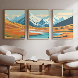 May include: Three framed landscape art prints depicting mountain scenes with blue, orange, and yellow hues. The artwork is displayed above a seating area with curved, cream-colored armchairs and a round wooden coffee table.