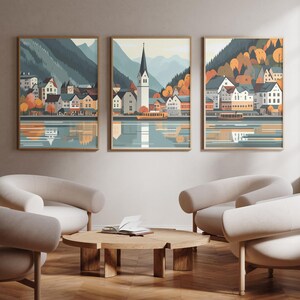 May include: Three framed illustrations of a small town with colorful buildings and a lake in the foreground. The illustrations are set against a backdrop of mountains and trees. The illustrations are in a modern style with a muted color palette.