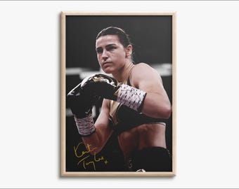 May include: A framed photograph of a boxer in a black sports bra and black boxing gloves with white hand wraps. The boxer is looking forward with a focused expression. The image features a gold signature in the bottom left corner of the print.