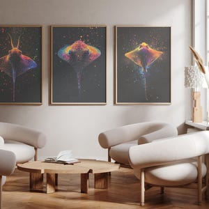 Op de afbeelding: Drie ingelijste wandkunstprints met kleurrijke pijlstaartroggen tegen een donkere achtergrond. Elke print toont een andere rog in een spetterende kunststijl met heldere tinten oranje, roze, blauw en geel, geplaatst in licht houten lijsten.