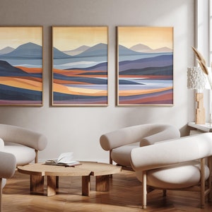 May include: Three abstract landscape paintings in muted tones of blue, purple, orange, and yellow, hanging on a light beige wall above a wooden coffee table and four white armchairs.