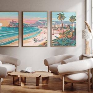 May include: Three framed illustrations depicting a beach scene with palm trees, buildings, and a sunset. The illustrations are in a modern, graphic style with bright colours. The illustrations are hanging on a wall in a living room with white walls and beige furniture.