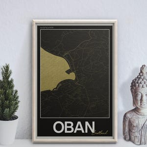 May include: Framed map art print of Oban, Scotland, featuring a gold and black color scheme. The map highlights the coastal area with detailed street lines. The word "OBAN" is displayed in white at the bottom, with "Scotland" below it.