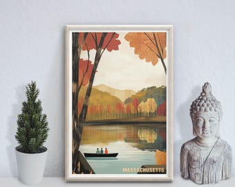 Op de afbeelding: Een ingelijste kunstdruk met een landschapsillustratie van een meer omringd door herfstbomen in oranje, rode en gele tinten. Een kleine boot met drie figuren drijft op het water. De tekst MASSACHUSETTS staat onderaan de afbeelding.