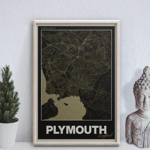 Może przedstawiać: Oprawiony wydruk mapy Plymouth w Anglii, w kolorze czarnym i złotym. Nazwa miasta jest wyświetlana białymi literami na dole. Małe dekoracyjne drzewko w białej doniczce i posąg Buddy znajdują się po obu stronach.