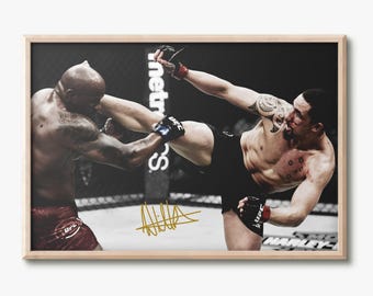 May include: A framed action photograph of two mixed martial arts fighters in a cage. One fighter delivers a high kick while the other blocks. The image features a gold signature on the lower portion and is enclosed in a light wood frame.