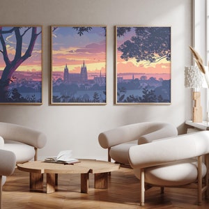 Może przedstawiać: Trzy oprawione wydruki krajobrazowe przedstawiające panoramę miasta o zachodzie słońca. Wydruki znajdują się w salonie z dwoma białymi fotelami i drewnianym stolikiem kawowym.
