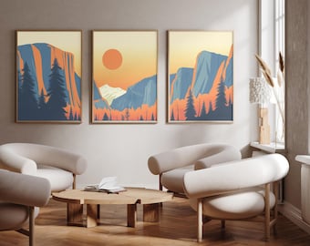 May include: A set of three framed wall art prints featuring a landscape illustration of mountains, pine trees, and a large orange sun. The artwork uses a color palette of blue, orange, and cream, depicting a scenic mountain range at sunset.