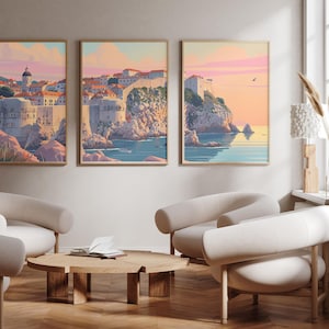May include: Three framed illustrations of a coastal city with a stone wall and buildings. The illustrations are in a muted colour palette of pink, blue, and green. The illustrations are hung on a light beige wall above a wooden coffee table and three white armchairs.