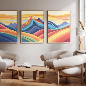 May include: A set of three framed wall art prints featuring a colorful landscape of rolling hills and mountains in shades of blue, green, yellow, orange, and red. The artwork displays layered, wavy patterns that create a sense of depth and movement.