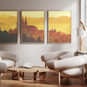 Może przedstawiać: Trzy oprawione wydruki krajobrazowe przedstawiające miasto z kościołem w oddali, na tle żółtego i pomarańczowego nieba zachodu słońca. Wydruki wiszą na jasnobeżowej ścianie nad drewnianym stolikiem kawowym i trzema białymi fotelami.