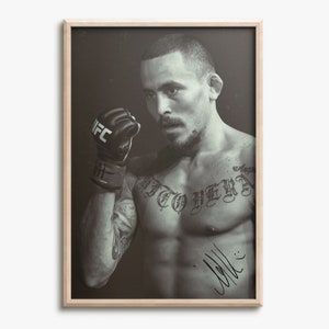 Puede incluir: Impresión en blanco y negro enmarcada que presenta un retrato de un artista marcial mixto. El luchador lleva un guante de la UFC y tiene tatuajes en el pecho y el brazo. La impresión está firmada en la esquina inferior derecha.