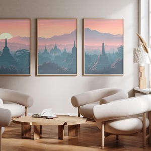 May include: A set of three framed wall art prints featuring a landscape of ancient stupas and temples at sunrise. The artwork displays a colour palette of soft pinks, oranges, and muted blues, depicting a misty mountain range and lush foliage.